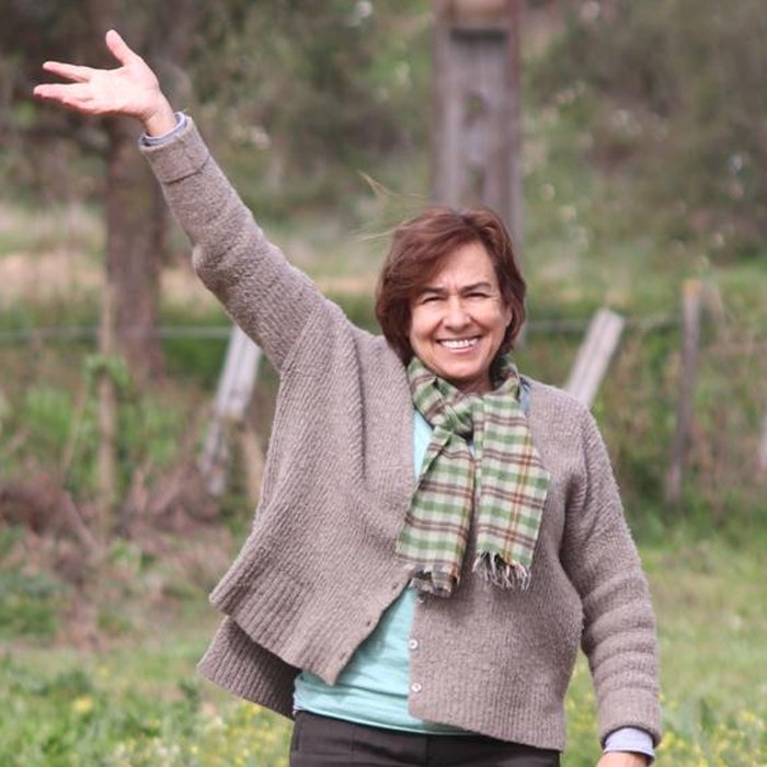 Maria João Abecasis smiling and waving as she walks across a field at Quinta do Pilar